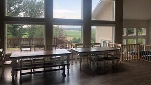 A spacious room with large windows offering views of a green landscape. There are wooden tables and chairs arranged for dining or socializing. - The perfect place for a vacation or reunion.  (Saint Anthony)