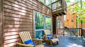 Eine Holzterrasse mit zwei Adirondack-Stühlen und einem Tisch, mit Blick auf eine bewaldete Gegend.