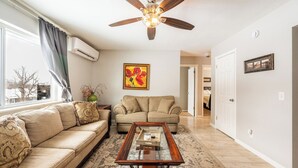 A living room with a beige sofa, a wooden coffee table, a ceiling fan, and a painting on the wall. - Walking distance historic downtown Sheridan (Sheridan)
