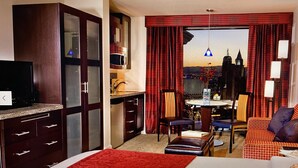Ett hotellrum med en säng, ett skrivbord, en stol, en soffa och utsikt över stadsbilden.