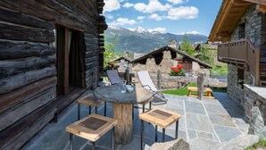 Una cabana de fusta amb un pati de pedra, seients exteriors i vista a la muntanya.