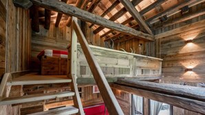 Interior rústic de fusta amb un llit amb zona superior, un sofà vermell i una escala que hi mena.