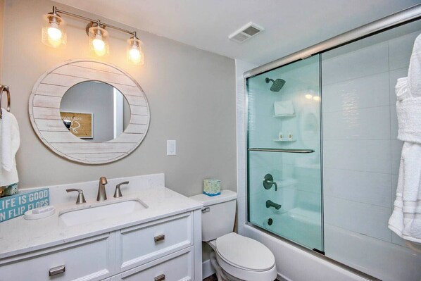 A bathroom with a round mirror, two sinks, a toilet, and a glass-enclosed shower.