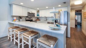 Una cocina moderna con armarios blancos, una isla central con taburetes de bar, electrodomésticos de acero inoxidable y un elemento decorativo azul.