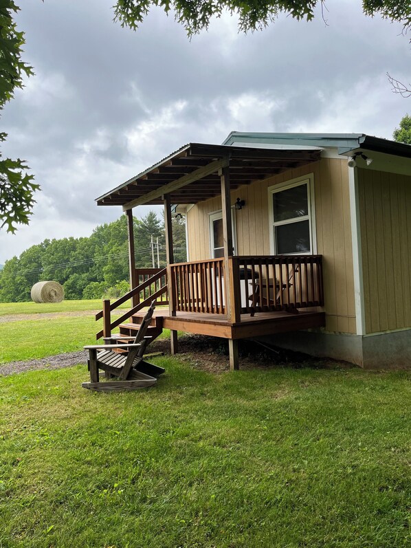 Een houten hut met veranda, een trap en uitzicht op een groen veld met hooibalen.
