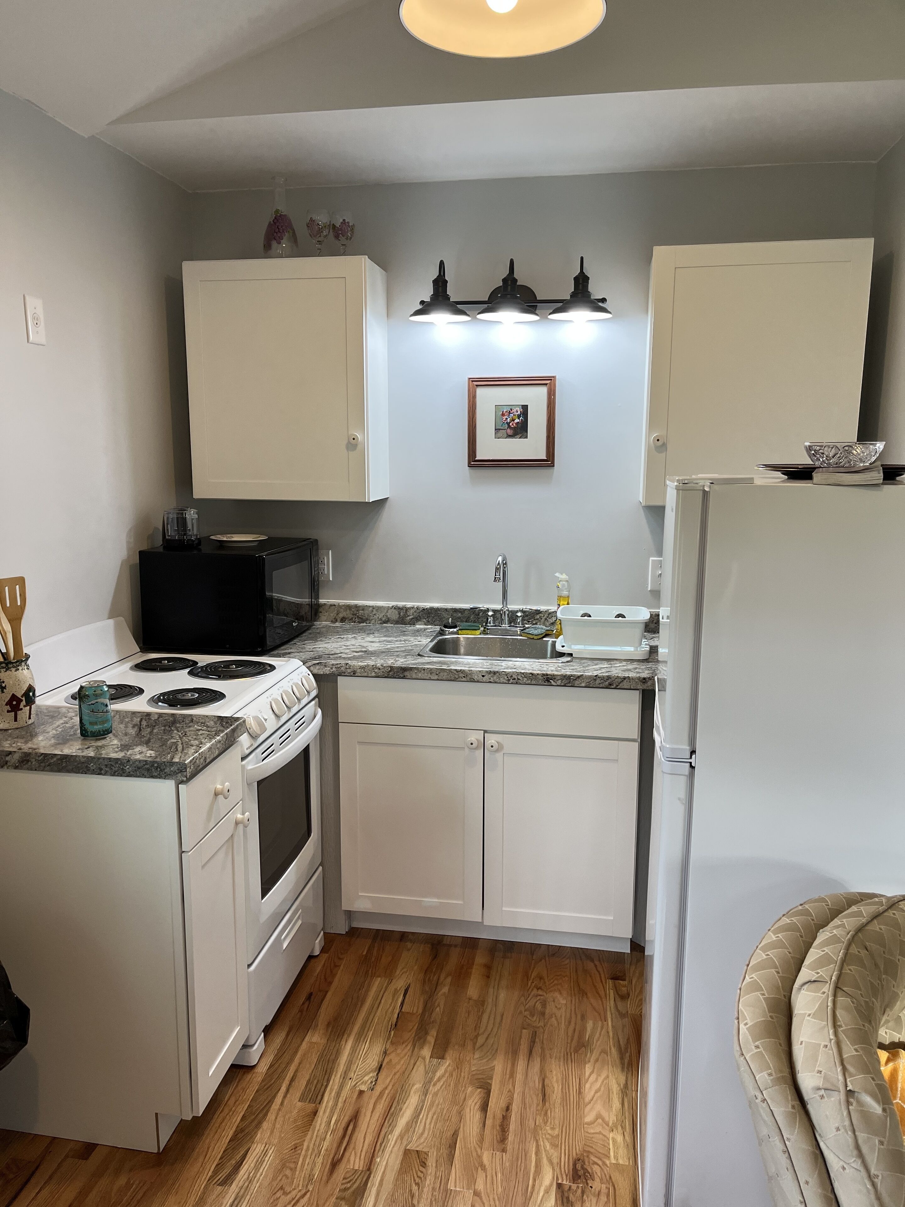 A compact kitchen with white cabinets, a stove, a sink, and a refrigerator.