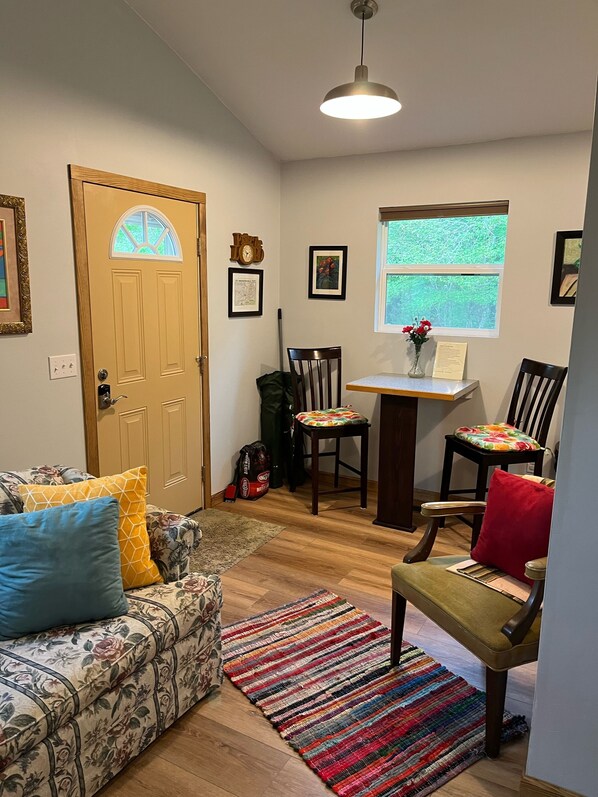 A cozy living room with a floral sofa, a wooden dining table, and a colorful rug. - Sleepy Bear #1. One Bedroom Cabin on the Blue Ridge Parkway in Floyd VA (Floyd)