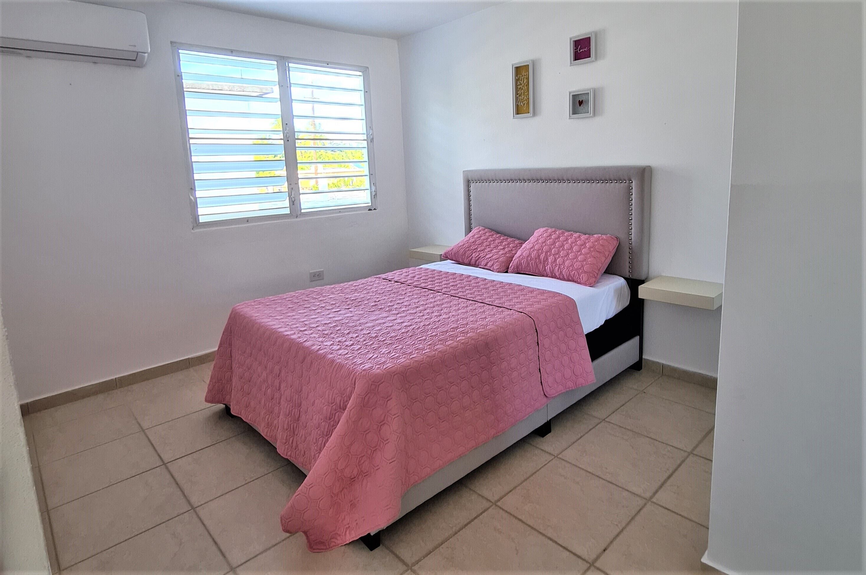 A bedroom with a bed, a window, and a wall-mounted shelf.