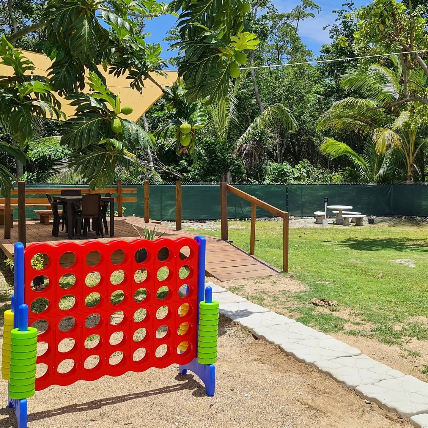 A playground with a red and green climbing structure, surrounded by palm trees and a grassy area.