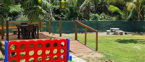 A playground with a red and green climbing structure, surrounded by palm trees and a grassy area.
