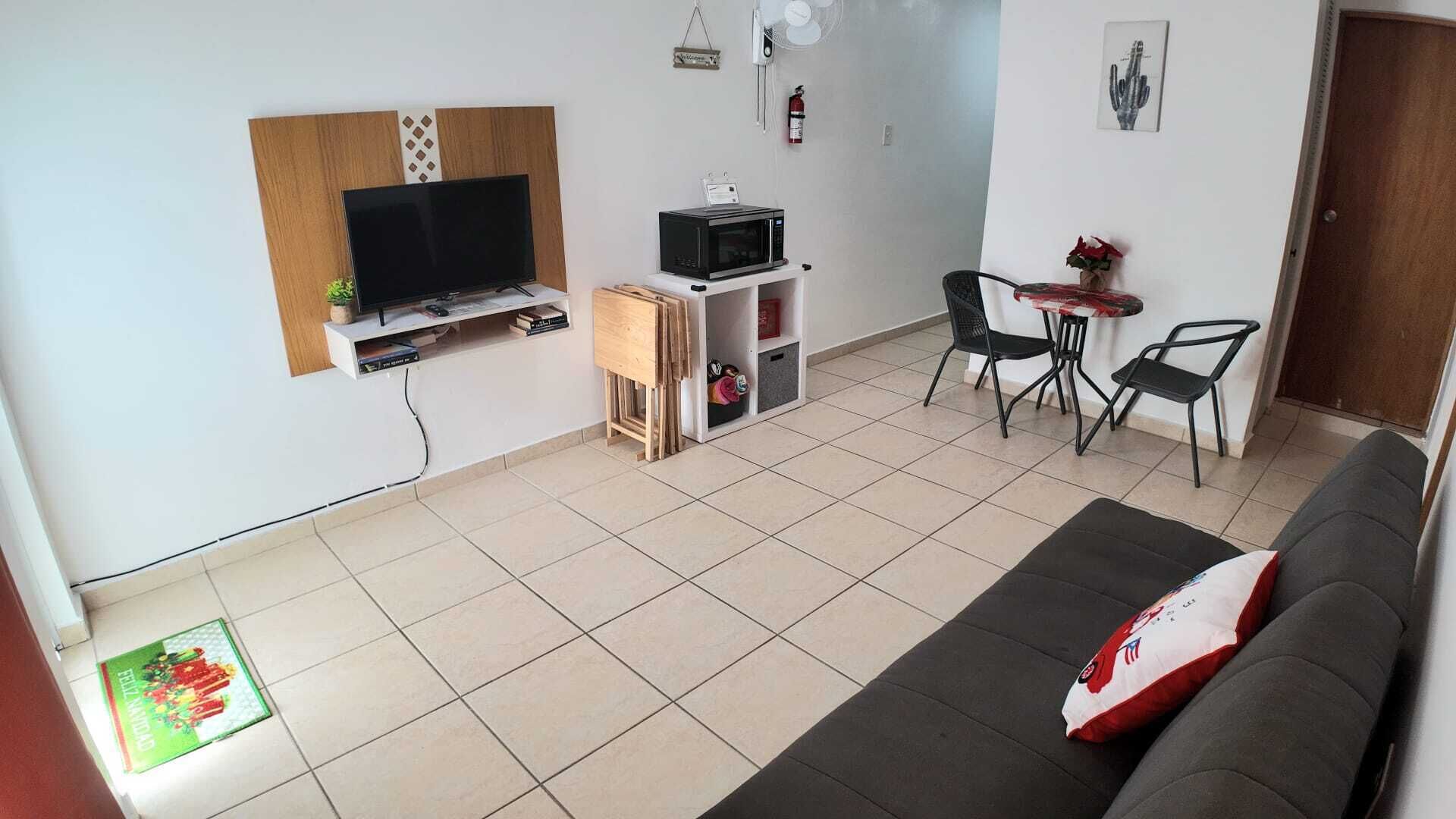 Ein modernes Wohnzimmer mit Fernseher, Mikrowelle und Essecke mit zwei Stühlen und einem kleinen Tisch.