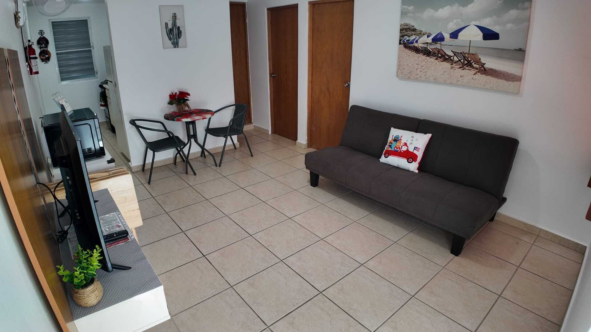 A living room with a sofa, a small table with chairs, a TV, and a plant.