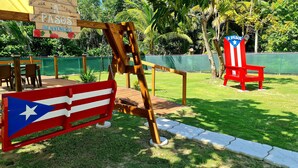 A wooden swing set with a flag design, a red bench, and a sign with 'A PASOS' and 'BIENVENIDOS' written on it. - 3 Luquillo Beach 2/B Apartment with Swimming Pool (Luquillo)