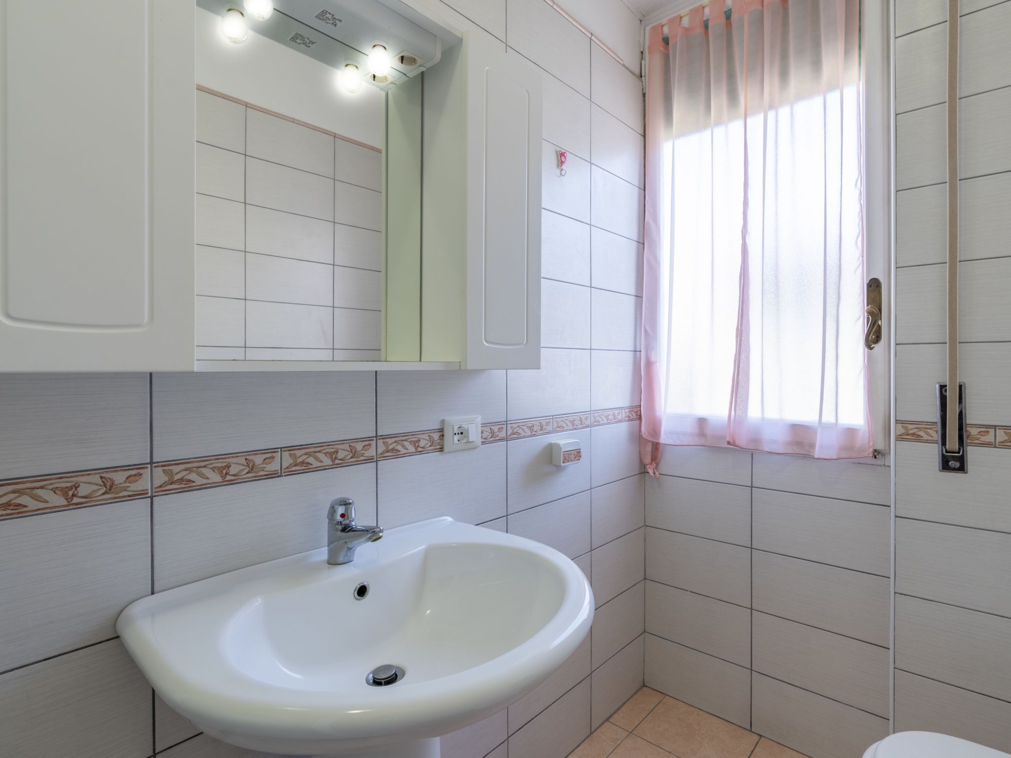 A bathroom with a white sink, a mirror, and a window with a pink curtain.