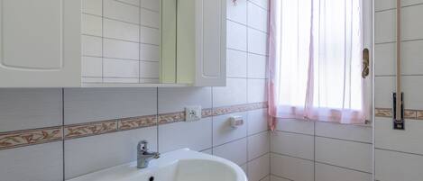 A bathroom with a white sink, a mirror, and a window with a pink curtain.