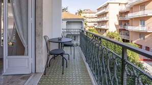 Un balcón con una mesa y sillas, vistas a edificios vecinos y un suelo con estampado verde.