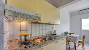 Een keuken met een inbouwfornuis, een gootsteen en een eethoek met een tafel en stoelen.