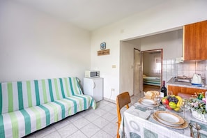 A compact living space with a sofa, a small kitchenette, a dining area with a table set for two, and a bed in the background. - Seaside Apt Basic 2 w/ Terrace, Vir, Croatia (Vir)