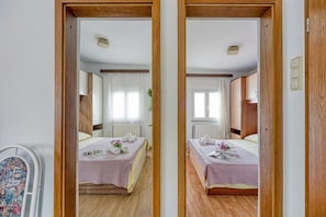 Ein Hotelzimmer, spiegelverkehrt, mit zwei Betten, einem Heizkörper und einem Fenster mit Vorhängen.