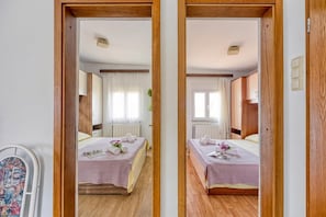 A mirrored view of a hotel room with two beds, wooden flooring, and a window with curtains. - Seaside Apt Basic 1 w/ Balcony, Vir, Croatia (Vir)