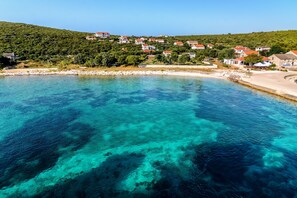 A coastal village with clear turquoise waters, houses on a hillside, and a sandy beach.