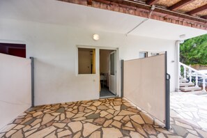 A covered outdoor area with a stone floor, a white wall, and a door leading to an interior space.