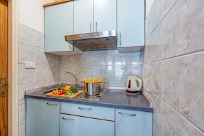 A kitchen with light blue cabinets, a stainless steel range hood, a sink with a faucet, a cutting board with vegetables, a pot of spaghetti, and a kettle.