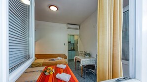 A hotel room with a bed, a small table with a vase, a window with blinds, and an air conditioning unit. - Seaside Studio Basic 3 w/ Terrace, Vir, Croatia (Vir)