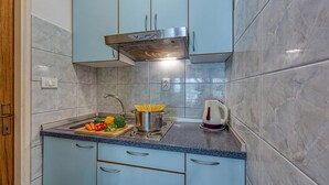A kitchen with light blue cabinets, a stainless steel range hood, a sink, and a countertop with vegetables and a pot. - Seaside Studio Basic 3 w/ Terrace, Vir, Croatia (Vir)
