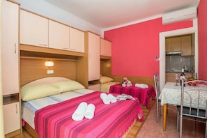 Un dormitorio con cama, mesitas de noche, una pequeña mesa con sillas y una kitchenette.