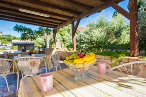 Un área de comedor al aire libre con una mesa dispuesta para dos, que incluye un frutero y tazas rosas.