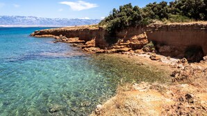 Un paisaje costero con aguas cristalinas, acantilados rocosos y una cadena montañosa distante.