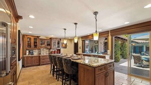 A spacious kitchen with a large island, wooden cabinets, and a view of the outdoor patio.