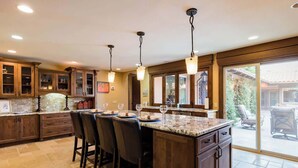 A kitchen with a large island, bar stools, wooden cabinets, and pendant lighting.