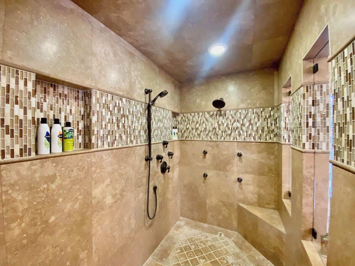 A shower area with a tiled wall, a handheld showerhead, and a floor with a geometric pattern.