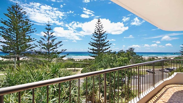 Ein Balkon mit Blick auf das Meer und den Strand, umgeben von Bäumen und einem Geländer.