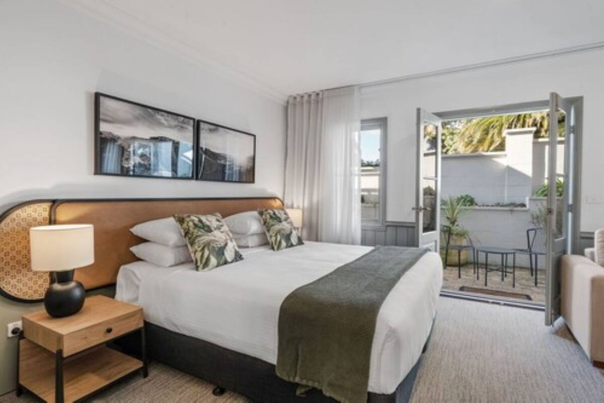 Une chambre d’hôtel moderne, équipée d’un lit, d’une table de chevet, d’une lampe et offrant une vue sur l’espace extérieur.