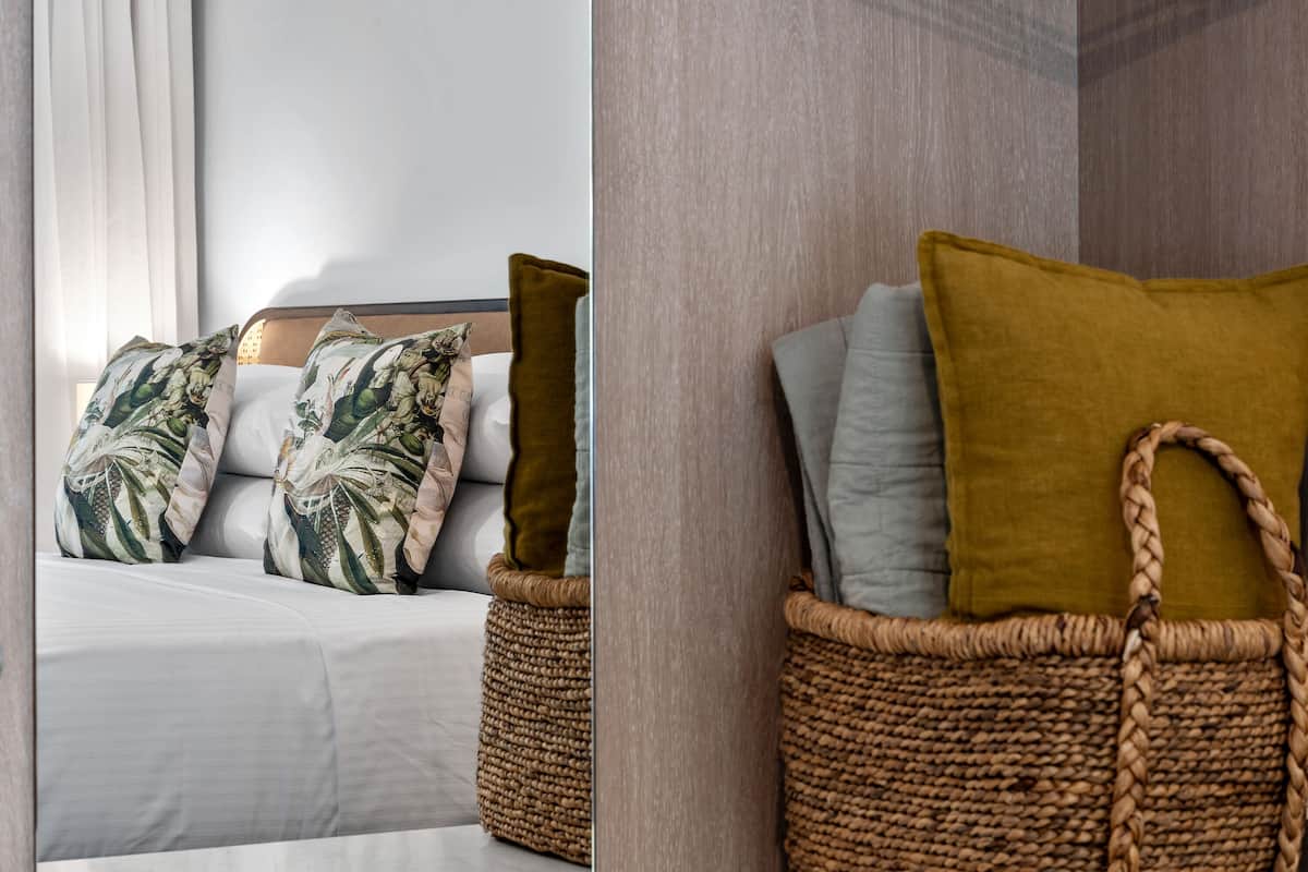 Un lit bien fait, agrémenté d’oreillers à motifs et d’un panier tressé placé à côté.