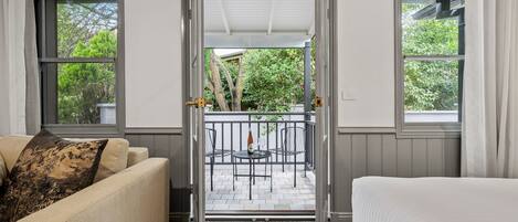 A room with a bed, a sofa, and a view of an outdoor patio with a table and chairs.