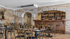 Un restaurante con paredes de piedra, una zona de bar con estantes llenos de botellas, y varias mesas y sillas.