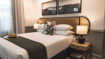 Una cama bien hecha con una manta verde, dos lámparas de noche, un sombrero sobre la cama y dos cuadros enmarcados en la pared.