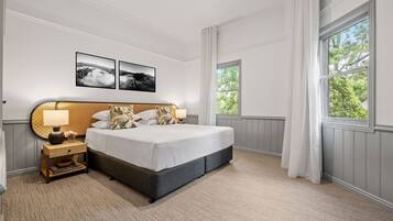A neatly arranged bedroom with a large bed, a bedside table with a lamp, and two framed pictures on the wall.