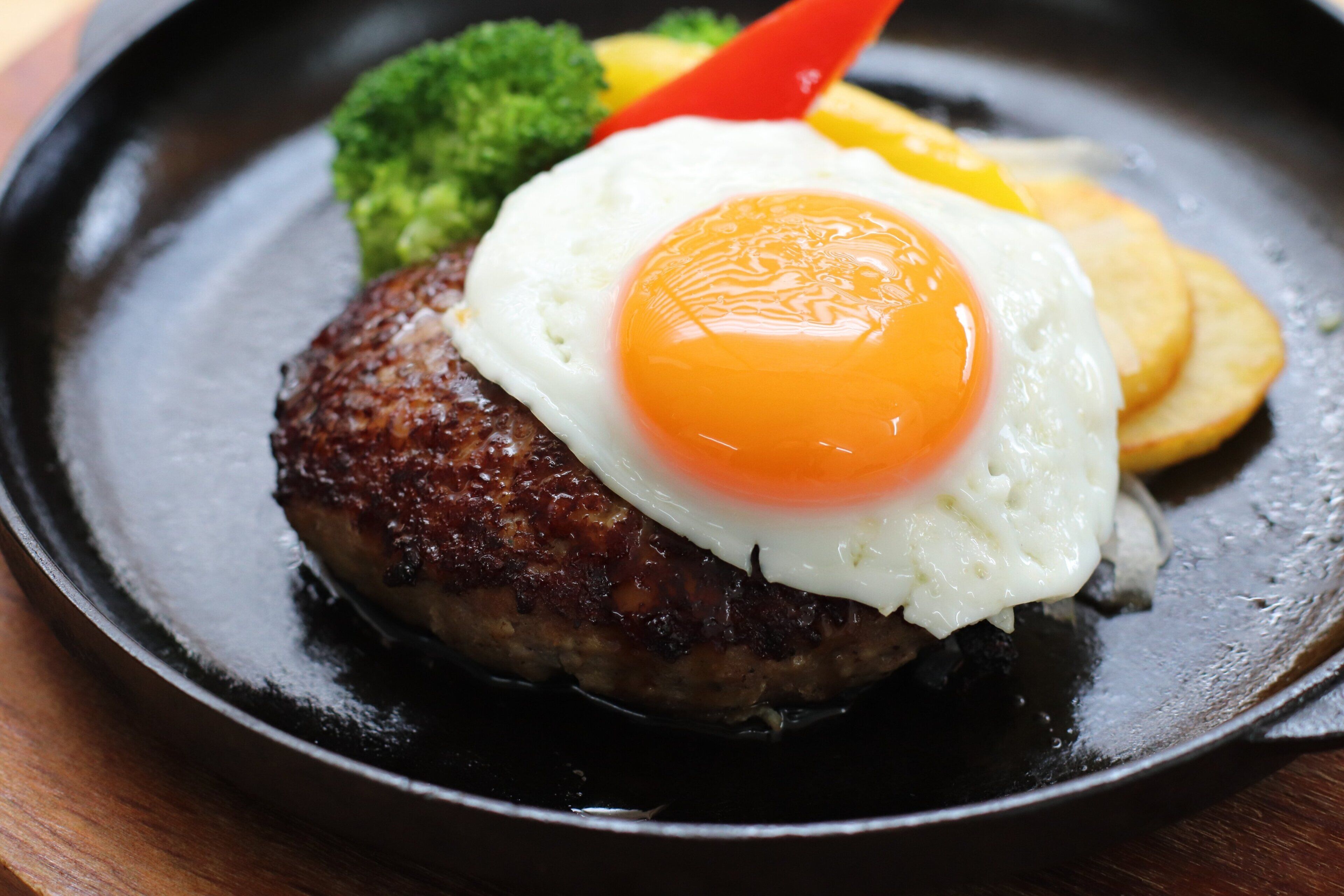 Gros plan d’une assiette de petit-déjeuner avec un œuf au plat, des pommes de terre rissolées et des brocolis.