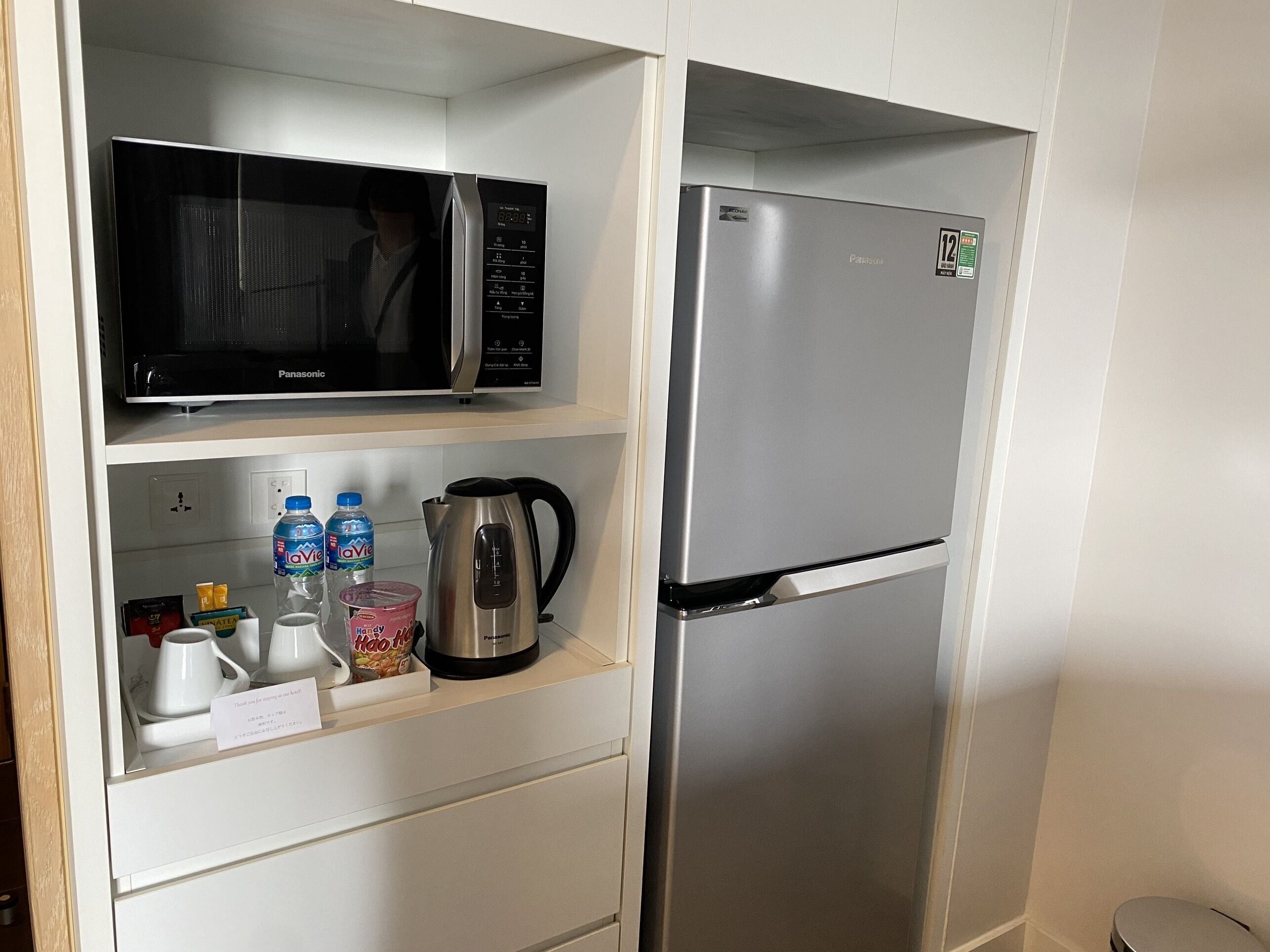 A compact kitchenette with a Panasonic microwave, a stainless steel refrigerator, and a coffee maker.