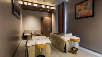 A spa room with two massage tables, a wooden cabinet, and a painting on the wall.