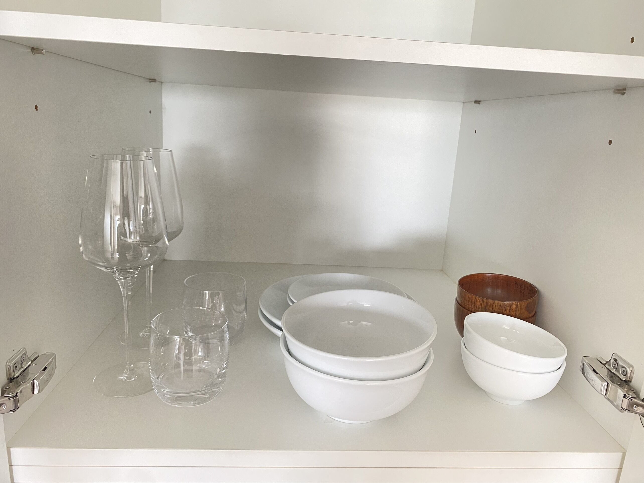 Una repisa blanca con cristalería transparente, platos blancos y un cuenco de madera.