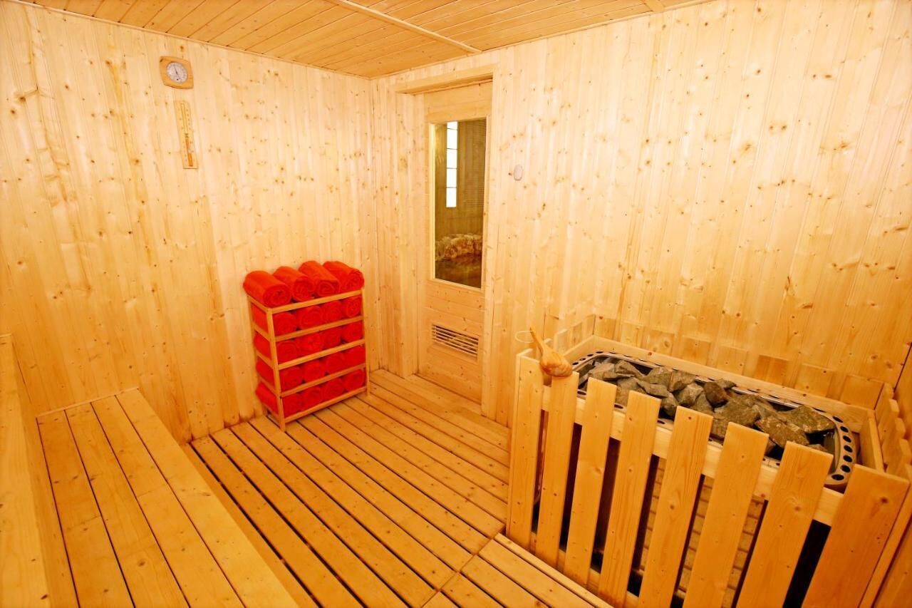 A sauna room with wooden walls and floor, a wooden bench, and a stack of red towels.
