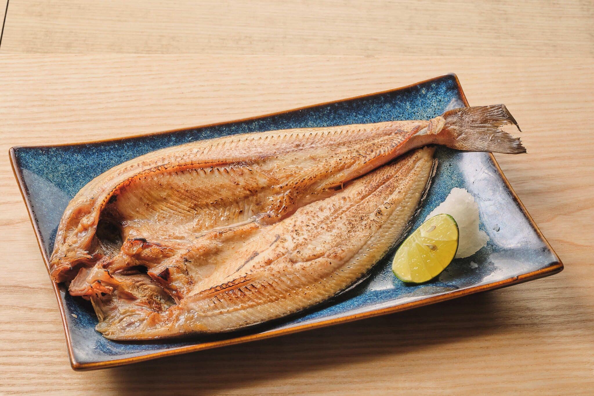 A fish on a ceramic plate with a slice of lime.