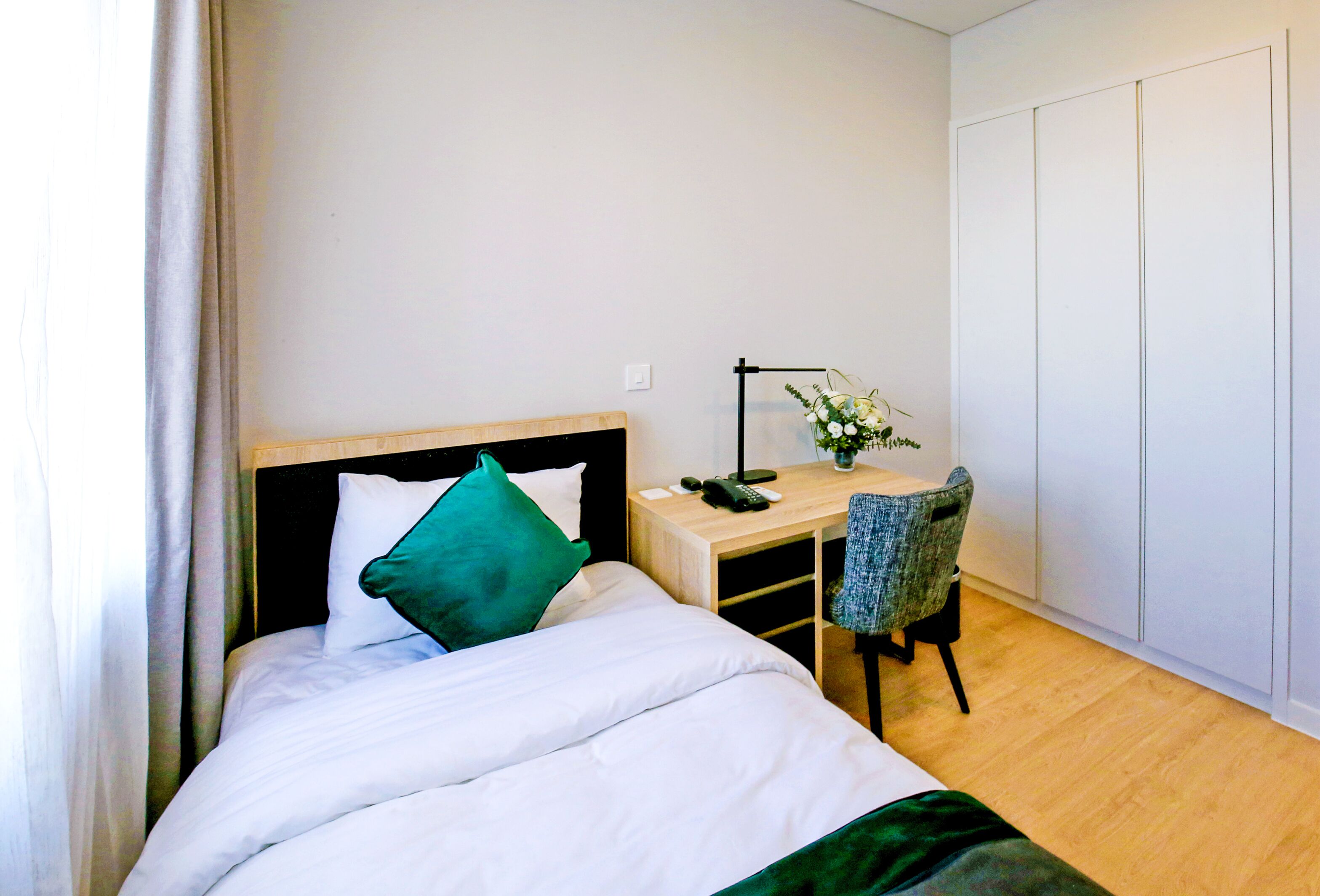 A hotel room with a bed, a desk, a chair, and a wardrobe.