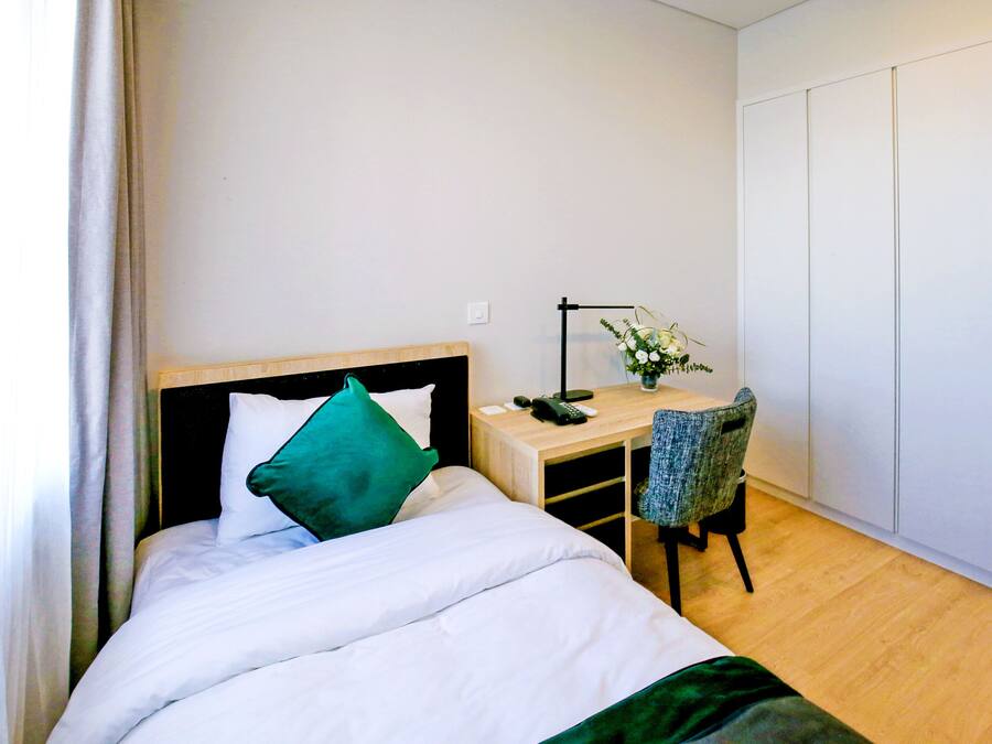 A hotel room with a bed, a desk, a chair, and a wardrobe.
